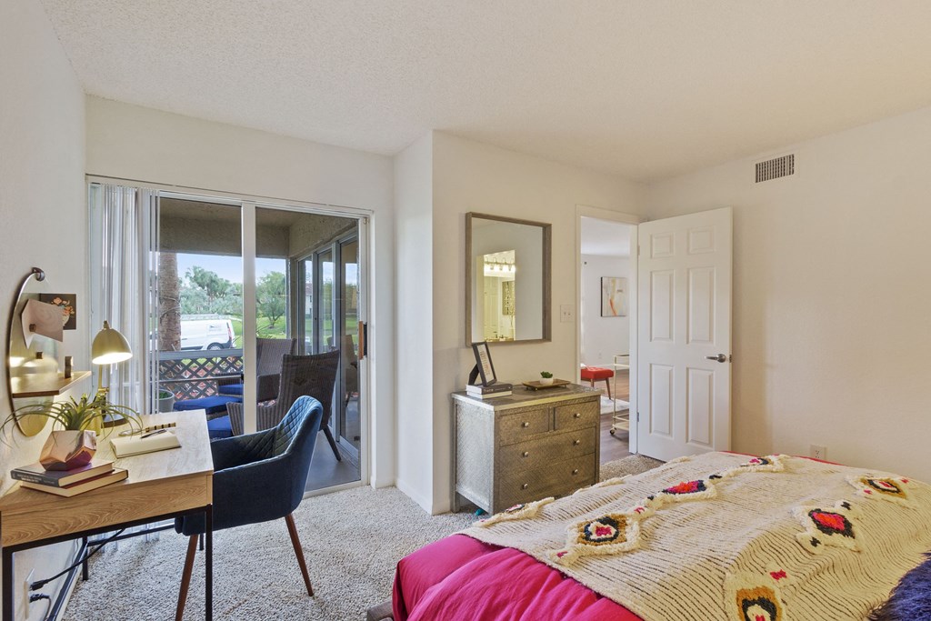 A bedroom with a bed, a chair, a desk, and a mirror.